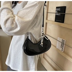 Detail of black croissant shoulder bag with glossy finish and pearl bow charm