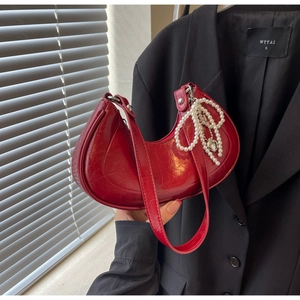 Detail of red crescent bag with glossy texture, pearl bow, and heart charm pendant