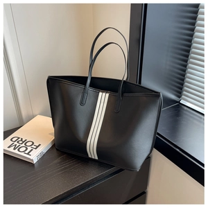 Close-up of a large black nylon tote bag with white stripes on a wooden desk