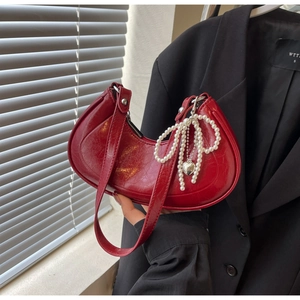 Detail of red crescent bag in glossy cracked leather with pearl bow and heart charm