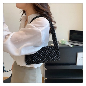 Side view of a black beaded shoulder bag worn by a model in a minimalist home setting