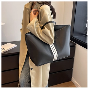 Detailed view of a large black nylon tote bag with white stripes on a model shoulder