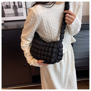 Detail of black bubble quilted shoulder bag texture on model in minimalist setting