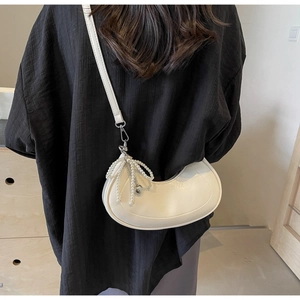 Detailed shot of white crescent shoulder bag featuring pearl bow and heart charm accents