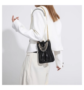 Detail of unique torso-shaped leather crossbody bag with layered metallic chains on model