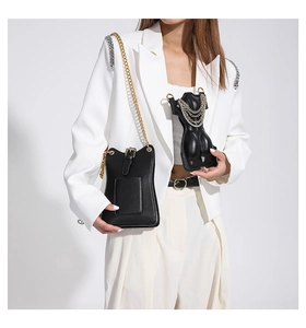 Close-up of minimalist black leather chain crossbody bag on white blazer