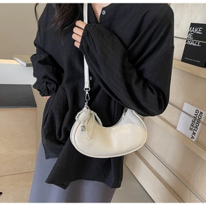 Close-up of a white patent leather half-moon bag with elegant pearl charm accessory