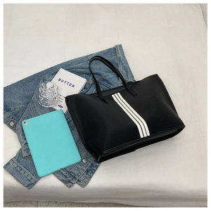 Detail view of a large black nylon tote bag with white stripes next to a tablet and book