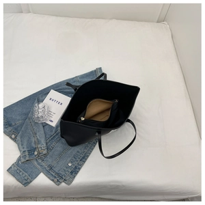 Top view of large black nylon tote bag with a brown zipper insert on white bedding