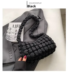 Detail shot of black bubble textured puff handbag displayed on grey suit and magazine