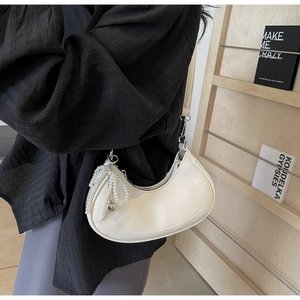 Detail of white half-moon hobo bag with pearl chain and metal heart pendant detail