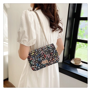 Detail of colorful graffiti chain bag with gold rotary lock worn by a model in white dress