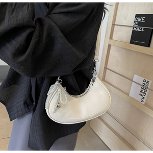 Detail of off-white crescent underarm bag featuring pearl charms and heart pendant