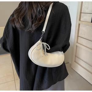 Detail view of cream crescent hobo bag featuring pearl bow charm and minimalist stitching