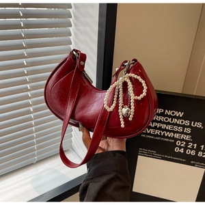 Detail of red crescent hobo bag featuring glossy texture and pearl heart charm decor