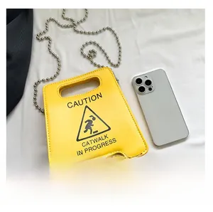 Creative yellow warning sign handbag with silver chain next to a smartphone for scale