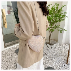 Sparkling pink heart-shaped crossbody bag with silver chain worn over a beige blazer
