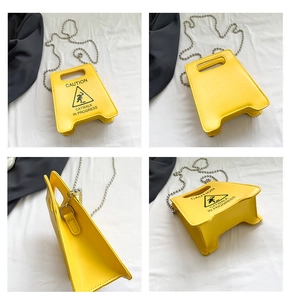 Detail view of yellow caution sign handbag showing multi-angle structure and ball chain