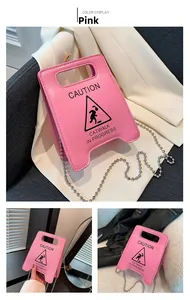 Close-up of bright pink shoulder bag with Caution graphic and silver ball chain
