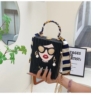 Detail of a black box bag with portrait print, striped handle, and gold chain strap