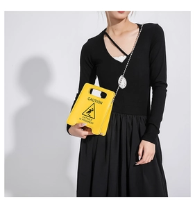 Close-up of a yellow caution sign shaped crossbody bag with metallic bead chain strap