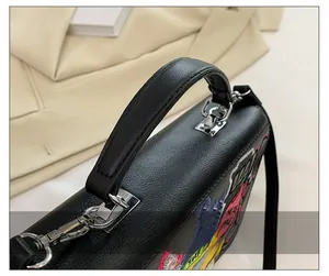 Detail of black lychee grain leather handbag featuring colorful embroidery patches and silver hardware
