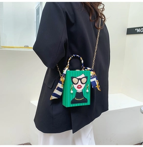 Close-up of green box bag with cartoon lady graphic, silk scarf handle, and gold chain