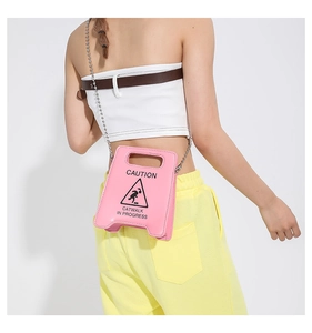 Pink caution sign crossbody bag with silver chain worn by a model at waist height