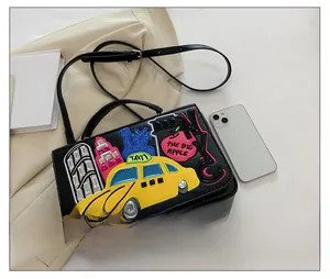 Close-up of NYC themed embroidery with yellow taxi and apple on black leather handbag