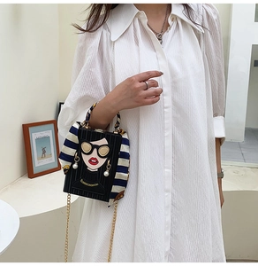 Detail of black box bag with cartoon face art and scarf-wrapped handle on a white shirt