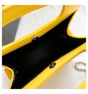 Detail of yellow crossbody bag showing silver magnetic closure and black lining