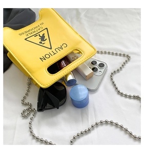 Top-down view of yellow Caution crossbody bag with silver chain and daily essentials inside