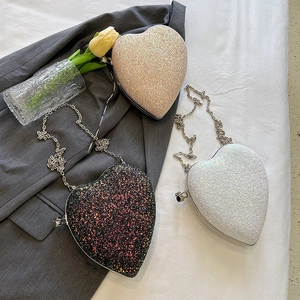 Three heart-shaped sequin evening bags in black, white, and champagne gold with chain straps