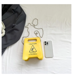 Detail of yellow caution sign shaped shoulder bag with silver chain on grey blazer