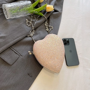 Pink heart-shaped evening clutch bag with sequins and silver chain on a casual setting