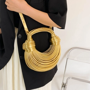 Artistic gold woven crescent handbag with knot details worn by a model in a modern room
