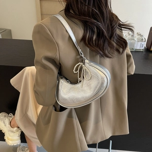 Metallic silver crescent hobo bag with pearl bow charm worn by model for commuter style