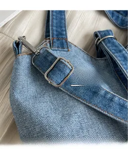 Detail of light blue denim fabric with orange topstitching and silver metal buckle adjustment