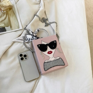Pink box crossbody bag with cartoon face and scarf-wrapped handle on neutral fabric