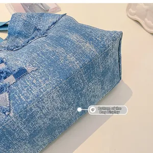 Detailed close-up of the reinforced bottom and raw edge denim texture of the blue tote bag