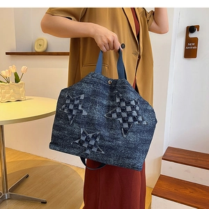 Detail of denim tote bag featuring three checkered star patches and blue ribbon handles