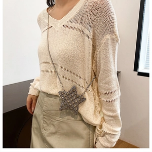 Detail of cream V-neck knit top with star-shaped crossbody bag on a female model