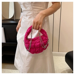 Detalle de bolso acolchado fucsia con cadenas metálicas sobre un vestido blanco