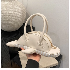 Close-up of dolphin-shaped cream handbag with striped trim and gold zipper details