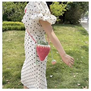 Outdoor shot of a handmade strawberry crochet crossbody bag with pink and white gradients