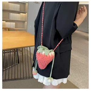 Detail of a handmade crochet strawberry crossbody bag with small leaf and charm accents