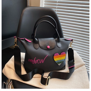 Detail of black handbag featuring a pink snap button and rainbow beaded heart patch