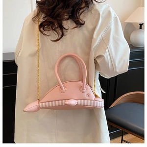 Pink whale-shaped shoulder bag with gold chain strap worn over a beige trench coat