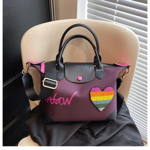 Detail of purple nylon handbag featuring a sequined heart patch and wide black strap