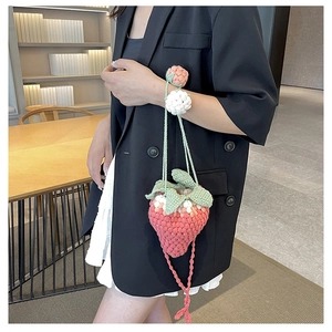Detail of a handmade crochet strawberry crossbody bag with pink yarn and green leaf accents